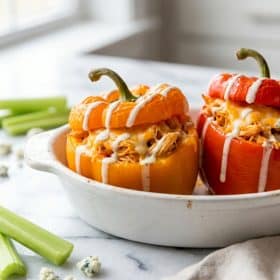 Buffalo chicken stuffed bell peppers in white baking dish with ranch drizzle