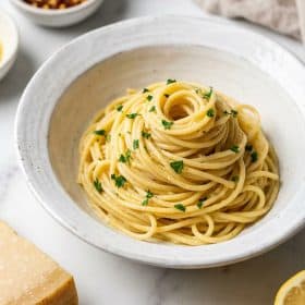 Garlic butter pasta with parsley and parmesan in a white ceramic bowl on marble surface