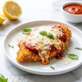 Single serving of oven baked chicken parmesan on a white plate with melted mozzarella and marinara sauce