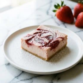Single strawberry cheesecake bar on white plate with powdered sugar