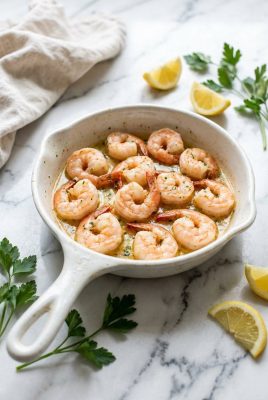 Garlic butter shrimp in a white ceramic skillet with parsley and lemon wedges