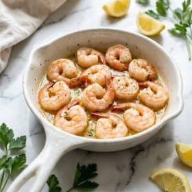 Garlic butter shrimp in a white ceramic skillet with parsley and lemon wedges