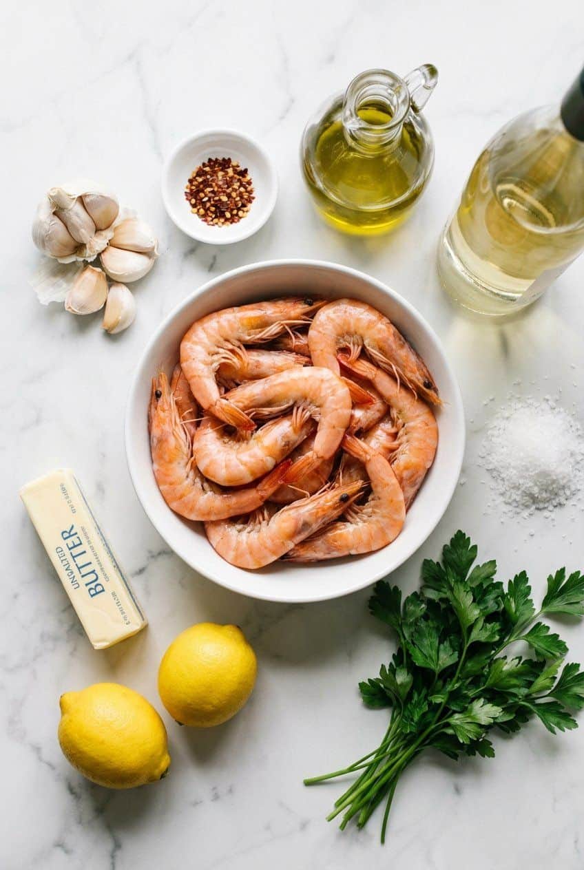 Raw ingredients for garlic butter shrimp in white bowls on marble