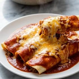 Close up of cheesy beef enchiladas with melted cheese and red sauce