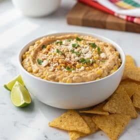 Elote corn dip in a white ceramic bowl on marble with tortilla chips