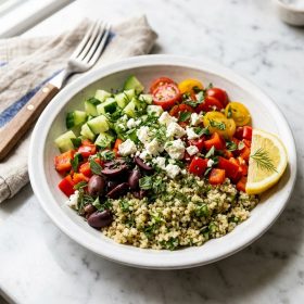Greek quinoa salad bowl with cucumber tomato olives and feta in white bowl