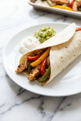 Close up of sheet pan chicken fajitas in a flour tortilla with sour cream and guacamole