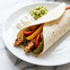 Close up of sheet pan chicken fajitas in a flour tortilla with sour cream and guacamole