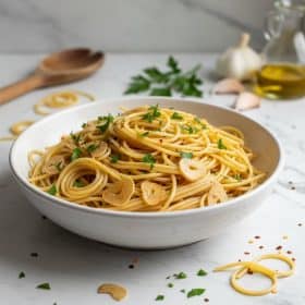 Spaghetti aglio e olio in a white ceramic bowl on marble with garlic and parsley